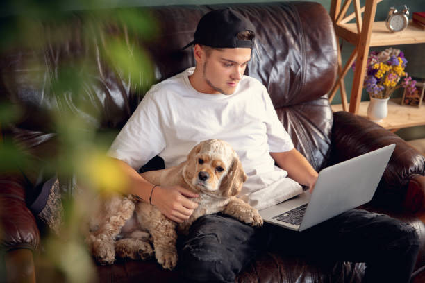 istock Young man working on laptop computer sitting at home with a dog pet and leaning during Coronavirus or Covid-19 quarantine 1288836337