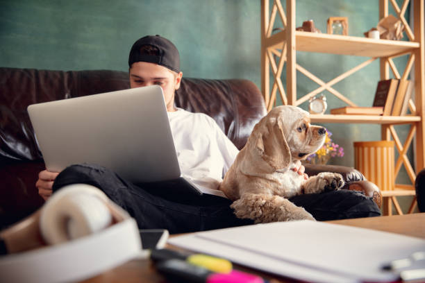 istock Young man working on laptop computer sitting at home with a dog pet and leaning during Coronavirus or Covid-19 quarantine 1288836339
