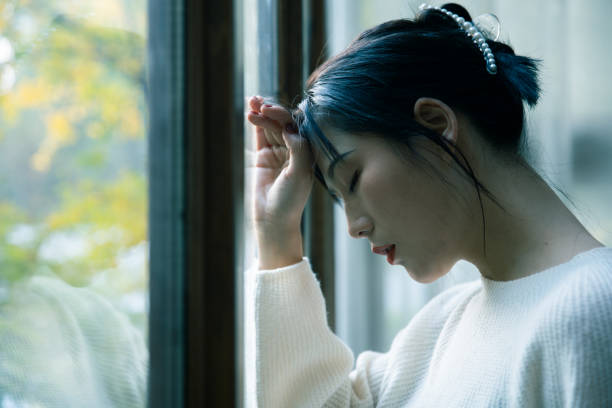 窓のそばに疲れた女性 - うつ病 女性 日本人 ストックフォトと画像