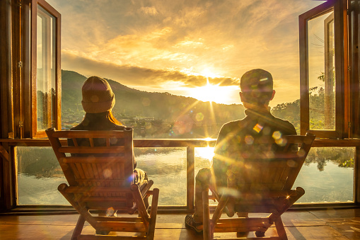 Happy young couple watching lake view at coffee shop in the morning sunrise, Ban Rak Thai village, Mae Hong Son province, Thailand. Travel, together and romantic concept