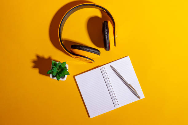 istock Desktop with yellow wireless headphones and an open notebook on a bright yellow background. 1288841038