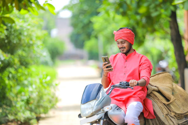 jeune fermier indien sur le vélo à moteur et utilisant le téléphone intelligent - sack burlap burlap sack bag photos et images de collection