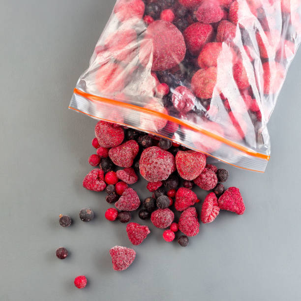 Frozen berries in the plastic bag and on a table, raspberry, strawberry, cranberry and black currant, top view, square stock photo