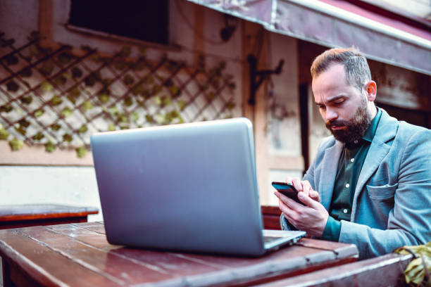 istock Businessman Using Smartphone While Working On Laptop In Coffee Bar 1288844450
