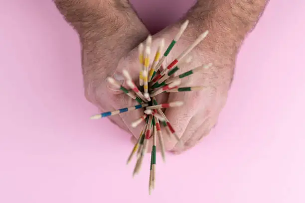 top view of hands holding mikado pick-up sticks against pink background