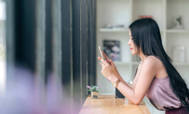 istock Young beautiful asian woman using smartphone while sitting at counter table in cafe, copy space. 1288848338
