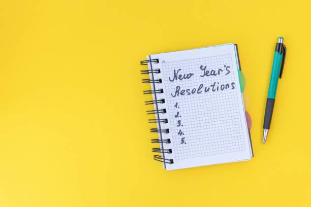 istock Writing in a notebook New Year's resolutions on yellow background with space for text. New Year's resolutions concept. Flat lay. Top view. 1288850235