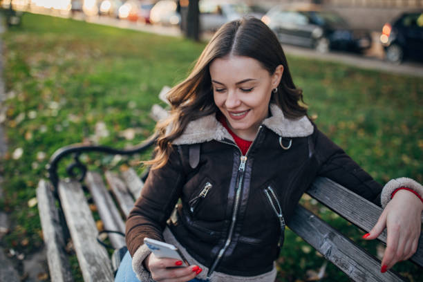 istock Beautiful woman using phone on bench in park 1288852766