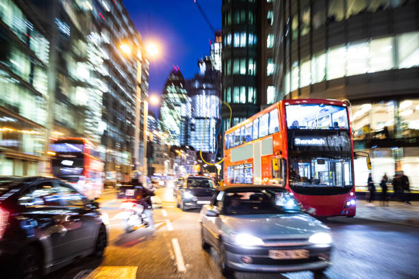 Bright car light trails dominate this view of the centre of London at night. In the background a red telephone booth.