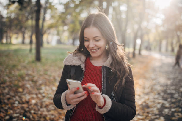istock Cheerful woman walking in autumn park and using smart phone 1288853379