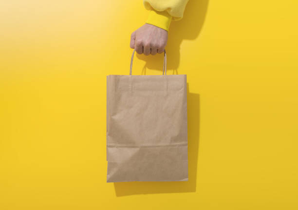 istock Hand holds paper bag on yellow background 1288854092