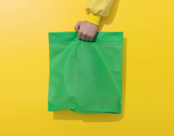 Hand holds green cotton bag on yellow background