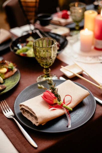 istock Empty black ceramic plate with a knife, fork on a napkin on a brown background, decorated with a red tulip, close-up. Elegant stylish table setting. 1288859568