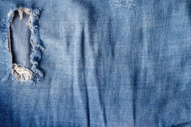 istock Blue torn jeans fabric texture. Distressed denim with hole and seam background 1288864037
