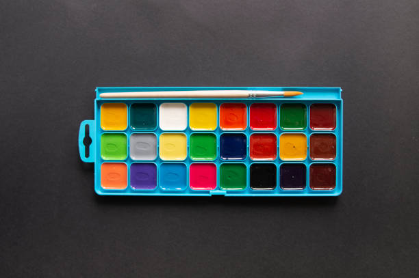 Bright multicolor watercolor paints and paintbrush in bare packaging on a black background. Top View, Flat Lay