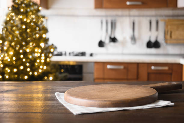 istock Wooden tabletop with cutting board and blurred modern kitchen with Christmas tree. 1288868666