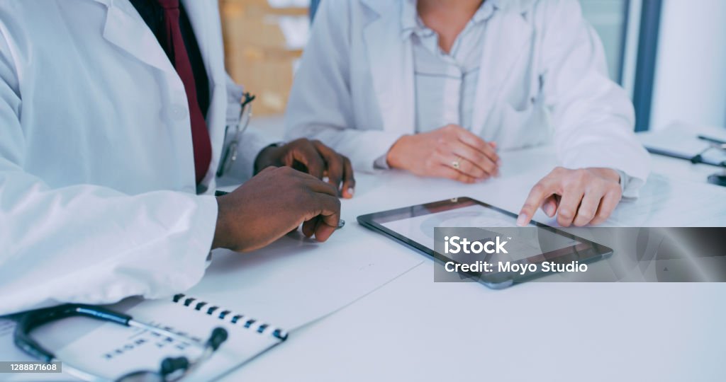Patient care just got a whole lot more streamlined Shot of two doctors using a digital tablet during a discussion in a clinic Healthcare And Medicine Stock Photo