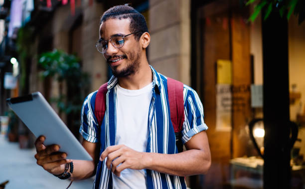 положительные темнокожие хипстер парень чтение дохода сообщение на цифровом планшете с помощью 4g роуминг подключение к интернету, улыбаяс - navigations стоковые фото и изображения
