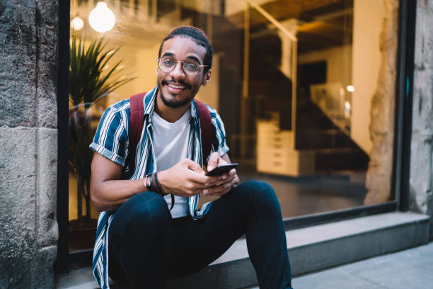 istock Bearded ethnic man browsing smartphone on stair and looking at camera 1288876077