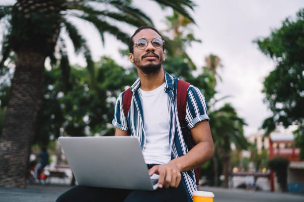 istock Focused ethnic man looking away while working on laptop outdoors 1288876134
