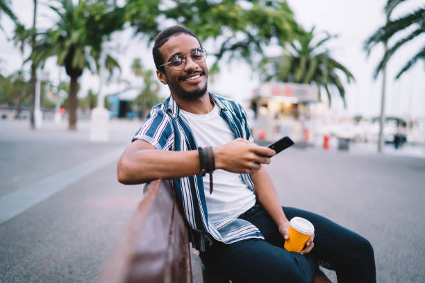 istock Confident man with smartphone and coffee sitting on bench 1288876136