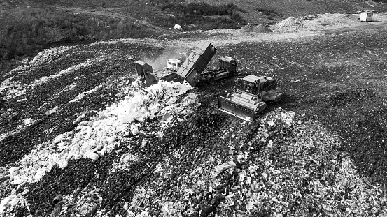 Top drone view of dump with different types of garbage. Trucks unloading waste. Landfill of big city. Black and white.