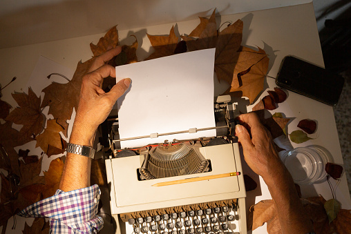 Top view of man's hands on a typewriter with autumn leaves , inspired writer