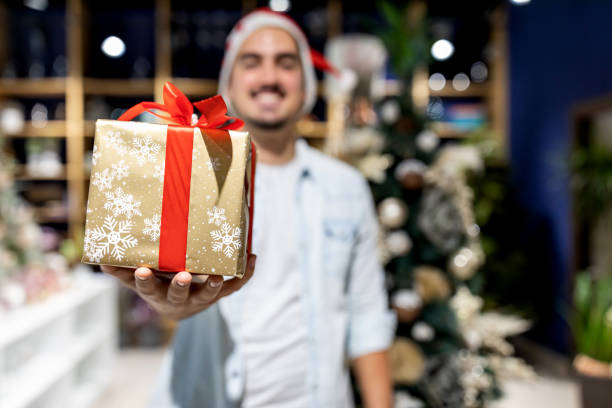 istock Happy young man in a Santa hat giving a Christmas present 1288881444