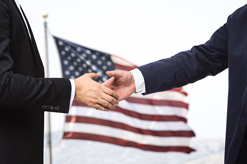 Two businessmen shake hands on the background of USA flag, partnership concept, close up