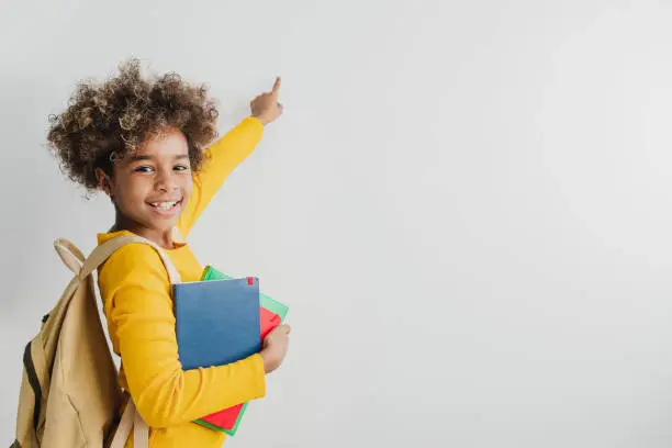 Photo of African American cute girl is holding school books an pointing on a copy space