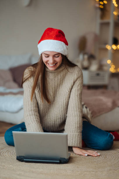 istock Female wearing santa hat while speaking with online friend on laptop 1288884140