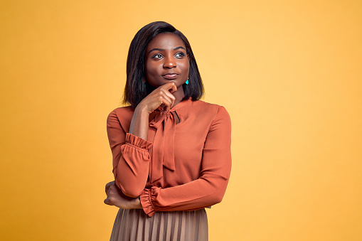Woman wearing isolated yellow background with hand on chin thinking about question, pensive expression. Smiling with thoughtful face. Doubt concept.