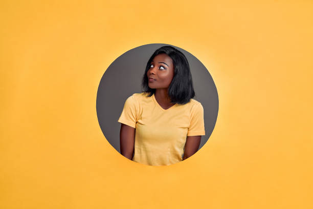 istock Beautiful young  woman in a round hole circle in orange background thinking about question, looking up, pensive expression. Smiling with thoughtful face. Copy space. 1288884252
