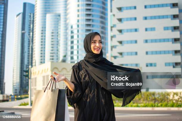 Beautiful Young Arab Muslim Woman In Abaya Clothes Holding Shopping Bags And Walking On The City Street Shopping Time Modern Skyscrapers In The Background Stock Photo - Download Image Now