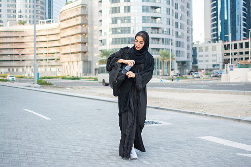 Young muslim woman in tradition Abaya clothes carrying sports bag and water bottle going to gym.