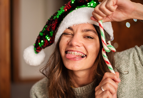 Portrait of a smiling young woman wearing a Santa hat sticking out out her tongue while holding some candy canes