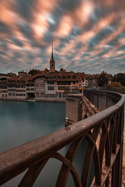 Long exposure of dramatic sunset sky clouds with focus on bridge hand railing and river Aare in Bern, UNESCO, Switzerland