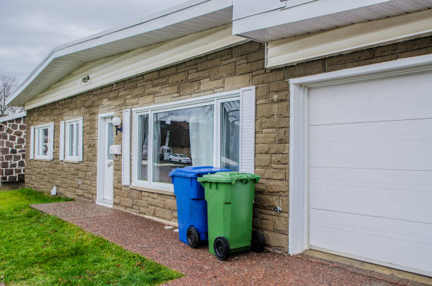 Old bungalow house seen from front yard. There is a garage and two garbage bins.