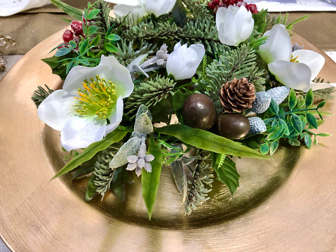 Stock photo showing a plastic spruce wreath on a gold plate as part of Christmas table place setting.