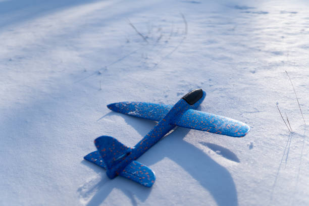 Blue hand throwing glinder airplane toy on snow on sunny day