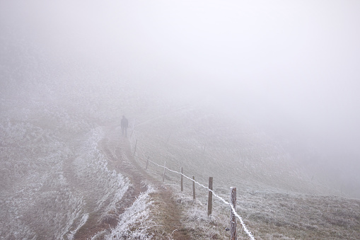 Magic landscape with hiking man in fog. Mountain trail covered with mist.