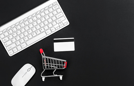 Computer keyboard, mouse, shopping cart and credit cards on black. Online shopping concept.