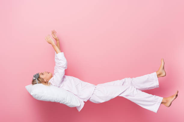 istock Young woman in pajamas lying on pillow on pink background 1288898024