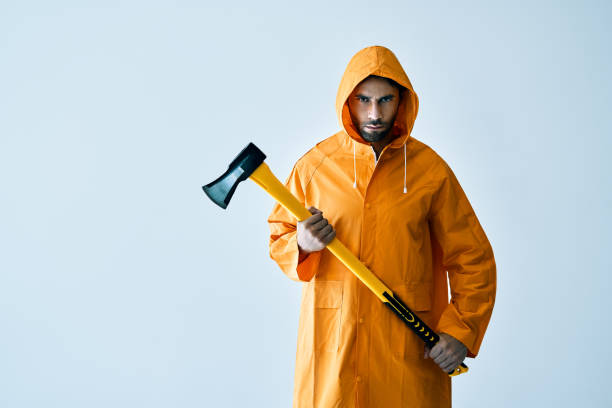 joven hombre serio con impermeable brillante sosteniendo un hacha grande en las manos con espacio de copia - axe murderer spooky men fotografías e imágenes de stock