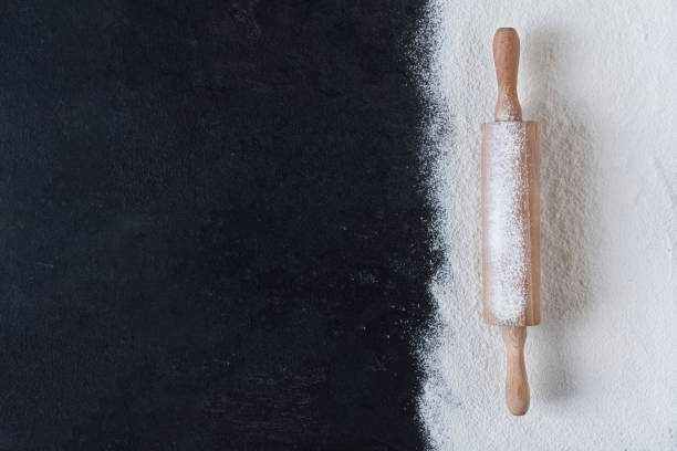 istock Sifted wheat flour over black surface with rolling pin top view. 1288903239
