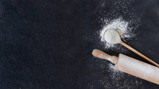 istock Wheat flour in a wooden spoon with rolling pin over black surface top view. 1288903242