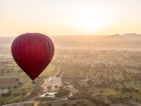 One big red ballon in the morning sunrise light over temples and lush green rainforest and rice fields agricultural fields