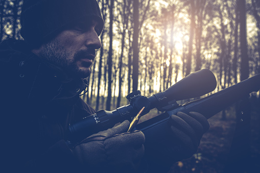 Close up image of male hunter loading riffle with led bullet while deer hunting in beautiful autumn forest in Denmark. During covid-19 related lockdown from work, more people spend time with their hobbies and pursuing outdoor activities and a healthy lifestyle.