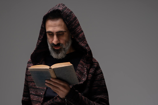 Man with a hood reading a book over gray background