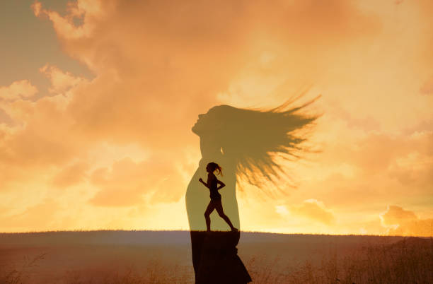Low angle silhouette image of young woman standing and contemplating phone against blue cloudy sky.